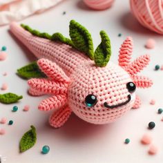 a pink crocheted stuffed animal with green leaves on it's head and two balls of yarn in the background