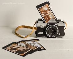 an old fashioned camera sitting on top of a table next to some pictures and a gold ribbon