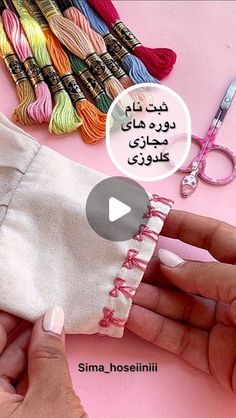 someone is sewing with scissors and thread on a pink surface next to several different colored yarns