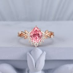 a pink diamond ring sitting on top of a white cloth covered box with a rose