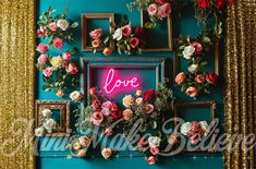 an arrangement of flowers and framed pictures on a blue wall with gold sequins