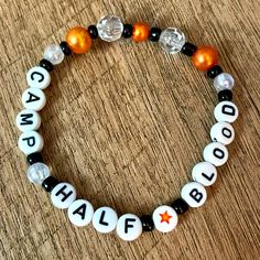 a black and white beaded bracelet with orange beads that says camp half blood on it