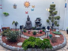 a buddha statue sitting in the middle of a garden with rocks and plants around it