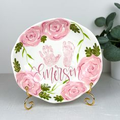 a personalized plate with pink roses and handprints on the front is next to a potted plant