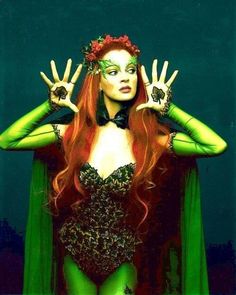 a woman with red hair and green makeup is dressed up as a witch holding her hands in front of her face