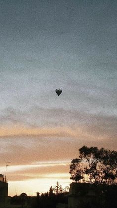 a hot air balloon is flying in the sky at sunset or dawn with trees and buildings behind it