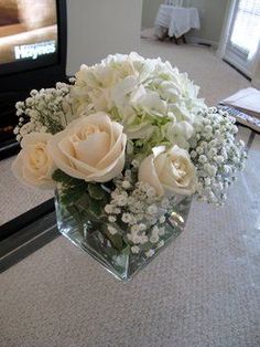 a vase filled with white flowers and baby's breath in front of a tv