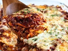 a wooden spoon scooping out some lasagna sauce from a casserole dish