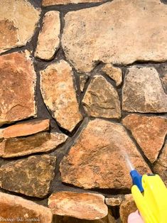 a person spraying water onto a stone wall with a yellow and blue sprayer on it