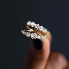 a woman's hand holding two gold rings with diamonds on them and the ring is in front of her face