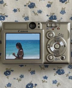 a digital camera sitting on top of a bed next to a flowered sheet with the image of a woman