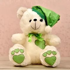 a white teddy bear wearing a green hat with paw prints on it's chest