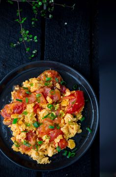 scrambled eggs with tomatoes and green onions on a black plate