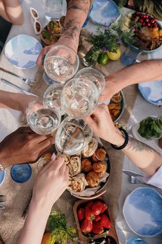 a group of people standing around a table with plates and bowls on it holding wine glasses