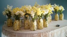 several mason jars with lemons and flowers in them on a lace tablecloth covered table