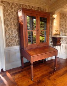 an old wooden table with glass doors in a room that has wallpaper on the walls