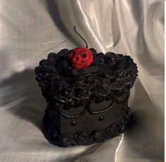 a small black box with a red rose on top sitting on a white cloth covered surface