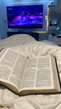 an open book sitting on top of a bed next to a flat screen tv in a bedroom