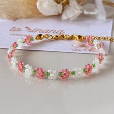 a close up of a bracelet on a table with flowers in the background and a card