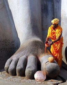 a man in an orange outfit sanding next to a giant foot