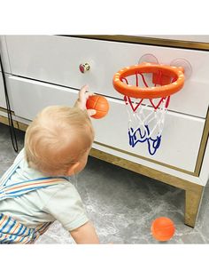 a toddler playing with an orange basketball in front of a white chest freezer