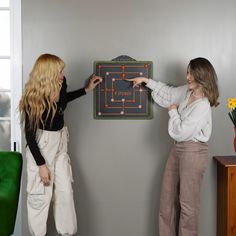 two women standing next to each other in front of a board