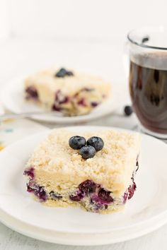 a piece of blueberry cake on a plate next to a cup of coffee