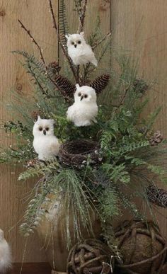 three white owls sitting on top of a wooden table next to pine cones and branches