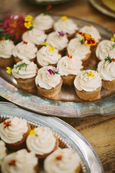 cupcakes are arranged on two platters with white frosting