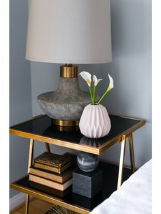 a table with a lamp, vase and books on it in front of a blue wall