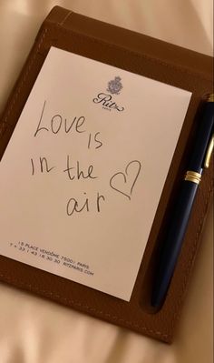 a notepad with writing on it and a pen sitting next to it that says love is in the air