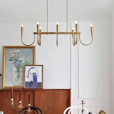 a dining room with chairs and chandelier hanging from the ceiling in front of a painting