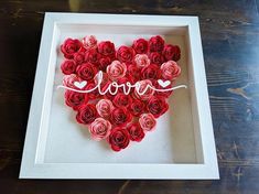 a heart made out of red roses with the word love written on it in a white frame