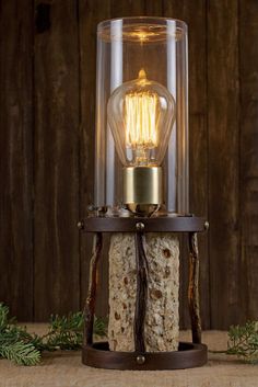 an old fashioned light bulb in a glass container on a stand with wood and rope