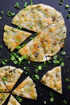 several pieces of pizza on a black surface with green onions and other toppings around it