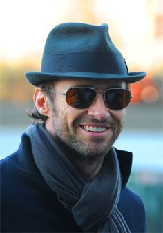 a man wearing sunglasses and a hat smiles at the camera while standing in front of another man