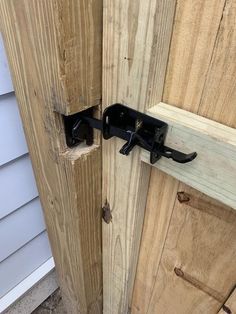 an open wooden door with a black handle on it's side and a white house in the background