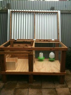 an outdoor area with a wooden structure and two green containers on the ground, in front of a metal fence