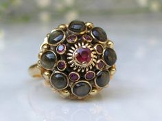 This ruby & black star sapphire harem ring can be considered big, bold and beautiful while still being elegant at the same time! Many people refer to it as a princess or harem ring, and also looks like a large gemstone flower! At the center top tier of attention is a Presidium tested ruby measuring approximately  0.17 carats that is held regally in place with 4 yellow gold prongs. The next tier of the ring design is all about the ruby colored stones! There is a total of 8 bezel set stones me Flower Gemstone Ring, Ornate Ruby Ring With Gemstone, Victorian Ring, Victorian Gold Ring With Ruby, Victorian Gold Rings With Ruby, Victorian 14k Gold Ruby Ring, Black Star Sapphire Ring Vintage, Etsy Engagement Rings Unique, Big Wedding Rings