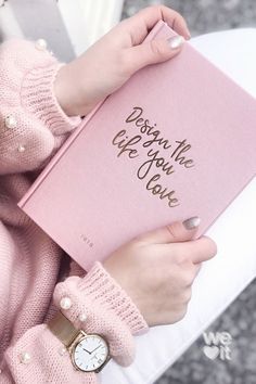 a woman holding a pink book with writing on it