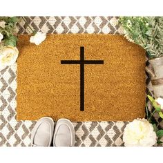 a door mat with a cross on it next to shoes and flowers in the background