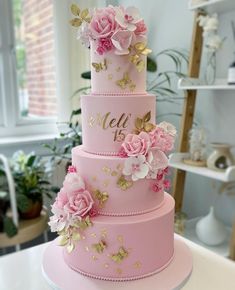 a three tiered pink cake with gold butterflies and flowers on the top, sitting on a table