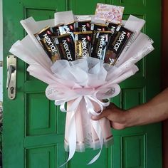 a hand holding a bouquet of chocolates in front of a green door with white ribbon