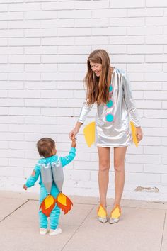 a woman holding the hand of a small child in front of a white brick wall