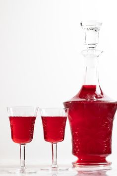 three glasses and a bottle with liquid in them sitting on a white surface next to each other