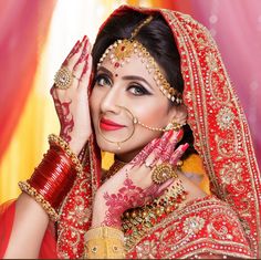 a woman in a red and gold bridal outfit holding her hands up to her face