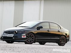 a black car parked in front of a white building with red rims on it