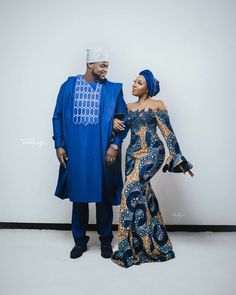 two people standing next to each other in front of a white wall wearing blue and gold outfits