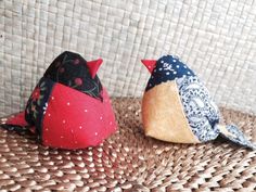 two small birds sitting on top of a woven tablecloth covered surface, one red and the other blue