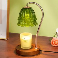 a green glass lamp sitting on top of a wooden table next to a flower vase